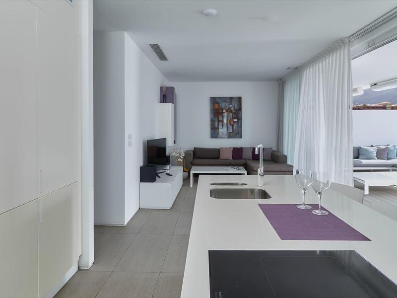 Cuisine ouverte moderne avec îlot, coin salon et grande fenêtre donnant sur la terrasse.