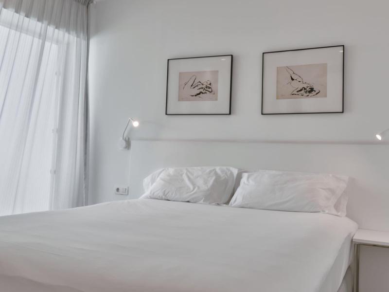 Chambre lumineuse avec lit blanc, oreillers et décoration murale minimaliste.