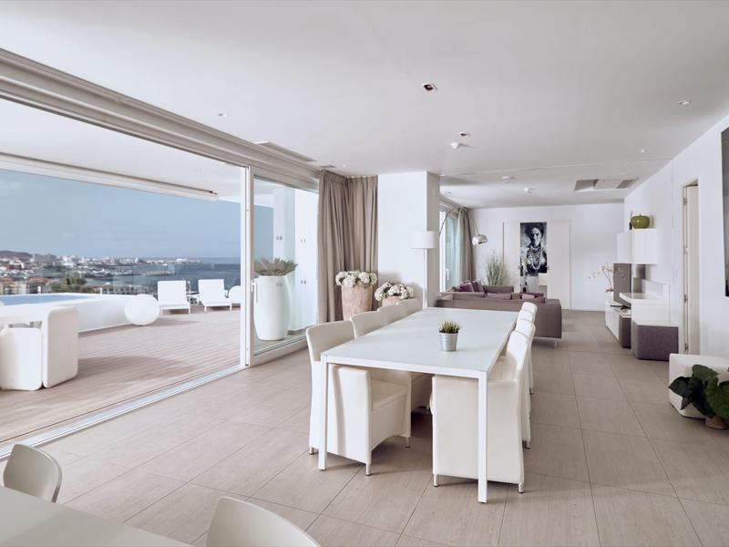 Espace de vie lumineux et moderne avec table, canapé et grande terrasse avec vue sur la mer.