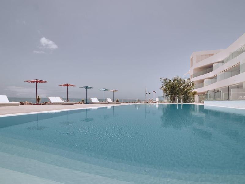 Piscine d'hôtel moderne avec chaises longues et parasols par une journée claire.