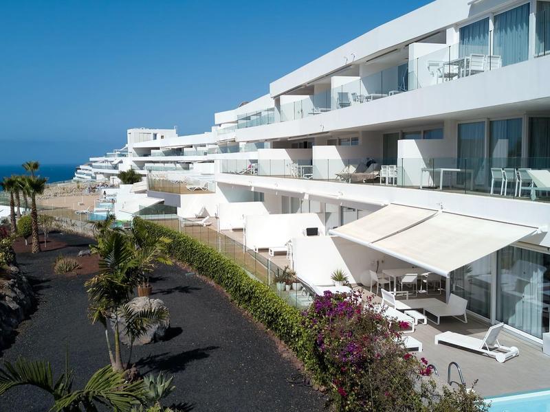 Complexe hôtelier blanc moderne avec terrasses et vue sur la mer sous un ciel bleu.