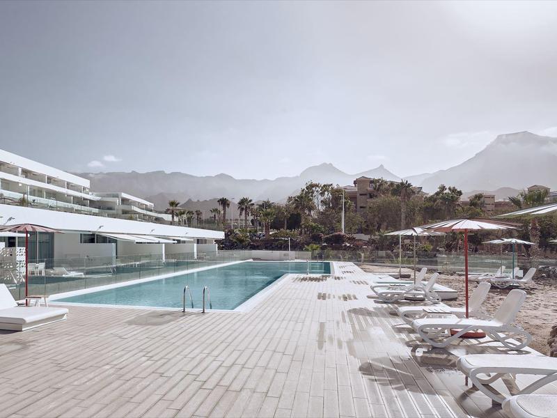 Espace piscine moderne d'un hôtel avec chaises longues et vue sur les montagnes en arrière-plan.