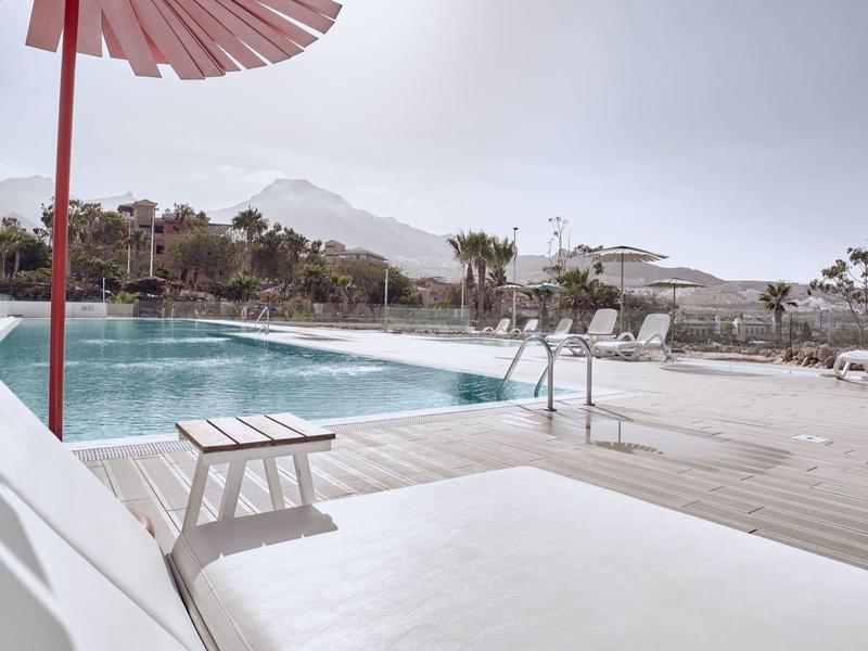 Espace piscine d'hôtel avec transats et parasols, montagnes en arrière-plan.