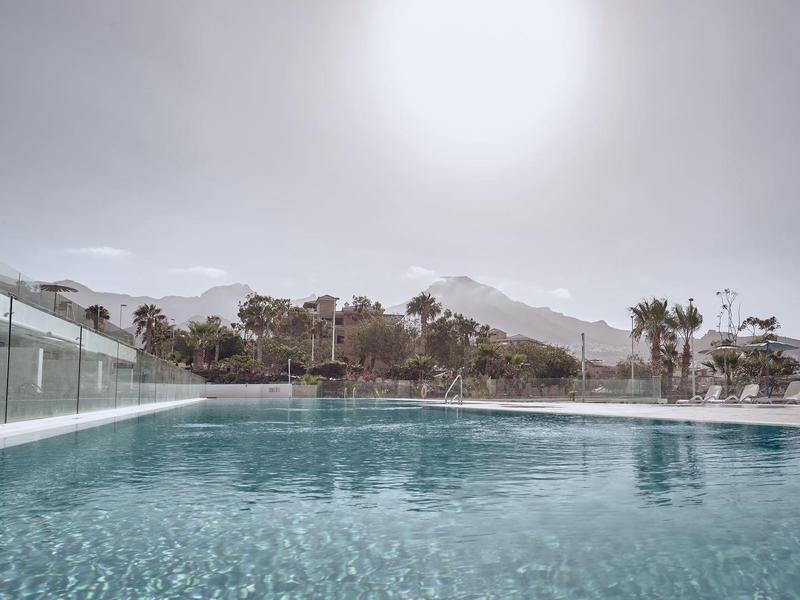 Piscine à l'eau claire entourée de rampes en verre avec des montagnes en arrière-plan
