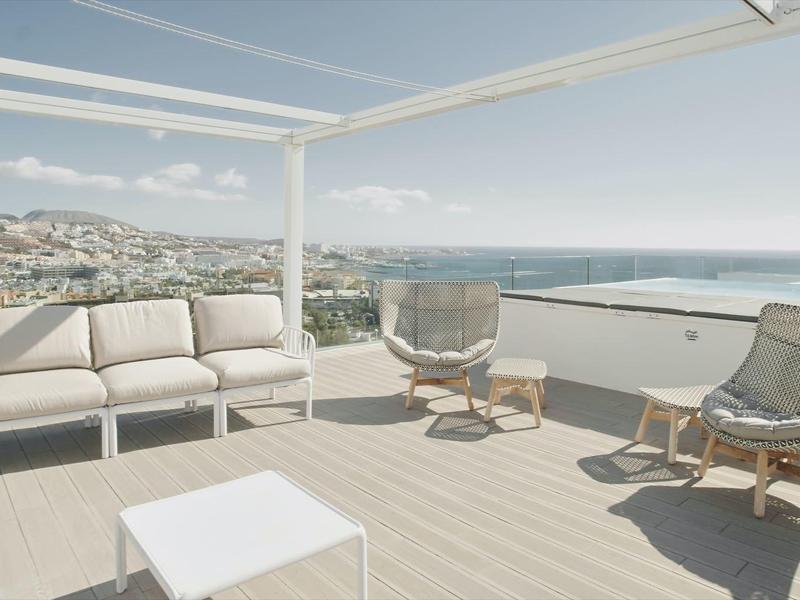 Terrasse moderne avec mobilier lounge élégant et vue sur la mer sous un ciel dégagé.
