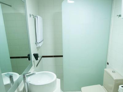 Kleines weißes Badezimmer mit rundem Waschbecken, Spiegel und halbtransparentem Duschvorhang.