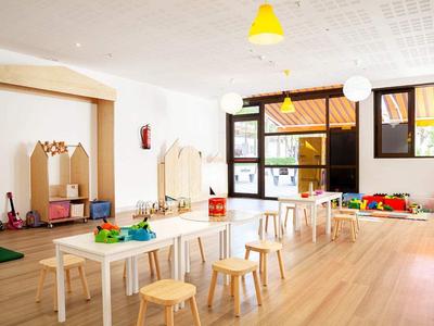 Heller, freundlicher Gruppenraum mit Stühlen, Tischen, Spielsachen und großen Fenstern.