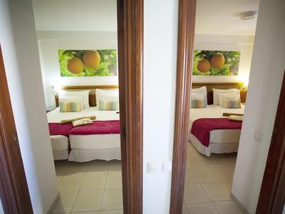 Zwei nebeneinander liegende Schlafzimmer mit weißen Wänden, Betten und Orangendekor an der Wand.