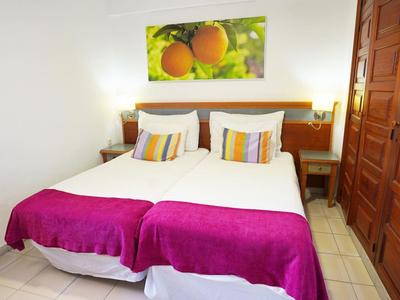 Gemütliches Doppelbett mit weißen Kissen, pinker Decke und Obst-Bild an weißer Wand.