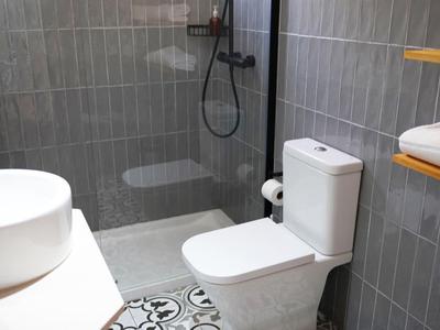 Modernes Badezimmer mit grauen Wandfliesen, weißer Toilette, rundem Waschbecken und Duschbereich.