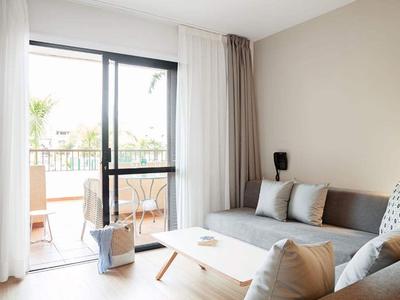 Jasny salon z szarą sofą i wyjściem na balkon z krzesłami.