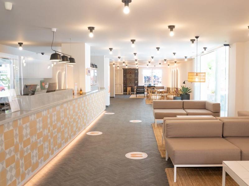 Helles Café mit modernen Sofas, Tischen, Pflanzen und großer Fensterfront, freundliche Atmosphäre.