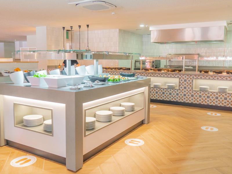 Modernes Buffet mit verschiedenen Speisen, helles Holzparkett und gedeckte Raumfarben.