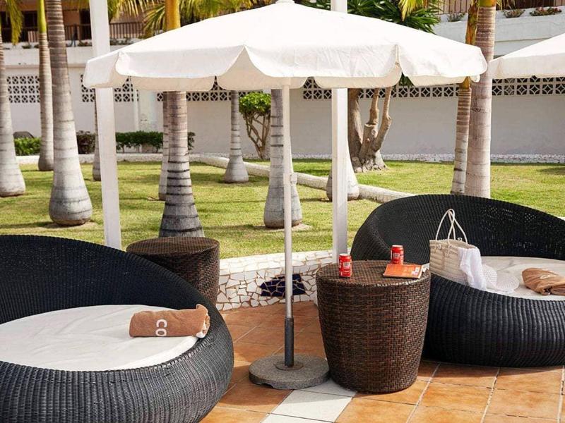 Garnitur mit schwarzem Rattan-Sofa und Tisch, weißer Sonnenschirm, braune Handtücher, Außenbereich.