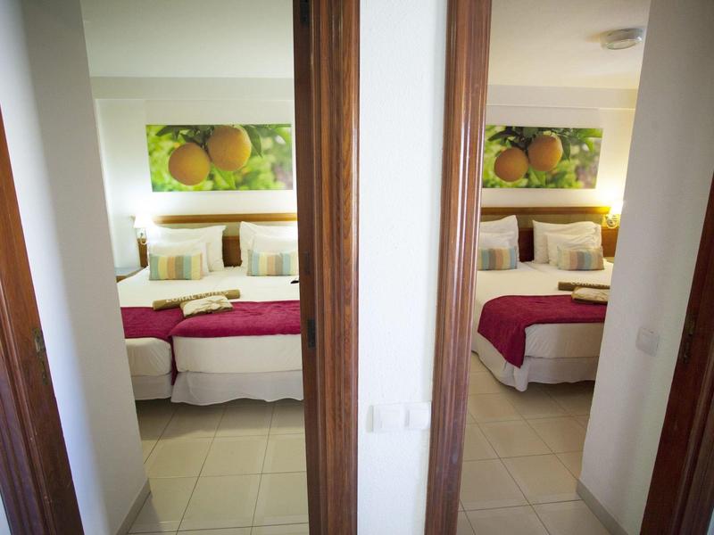 Zwei nebeneinander liegende Schlafzimmer mit weißen Wänden, Betten und Orangendekor an der Wand.