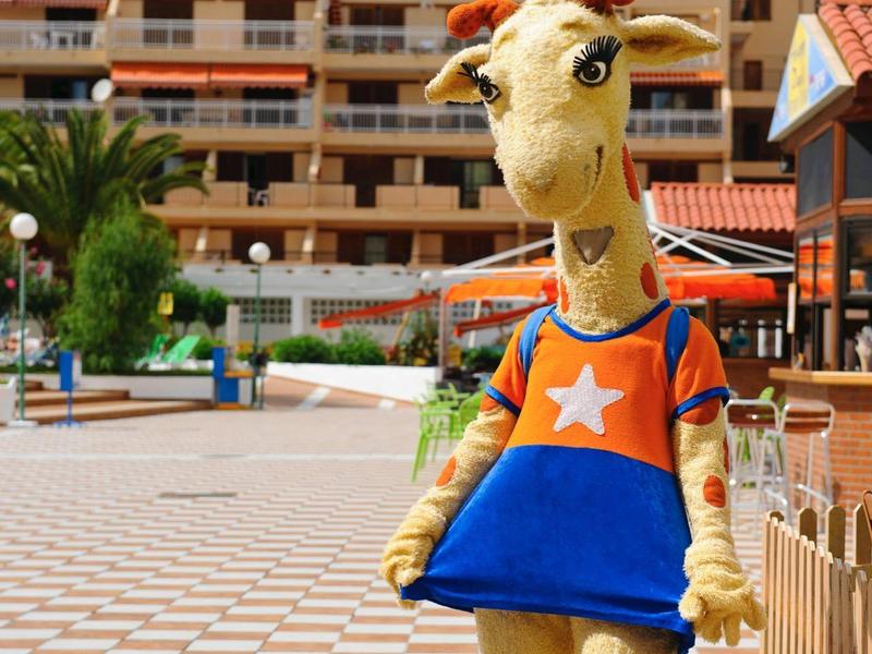 Große gelbe Giraffenfigur mit blau-orangefarbenem Kleid steht vor einem Hotelgebäude.