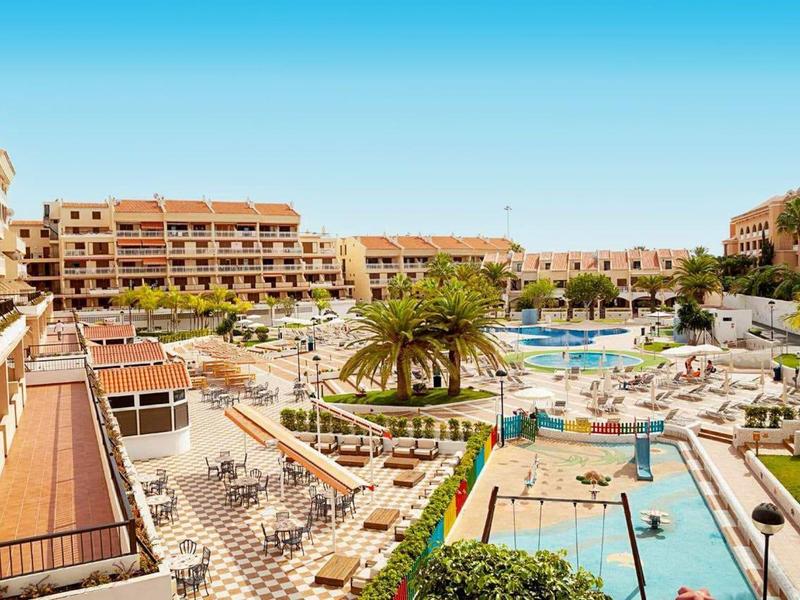 Großes Hotel mit mehreren Pools, Liegestühlen, Palmen und heller mediterraner Architektur.