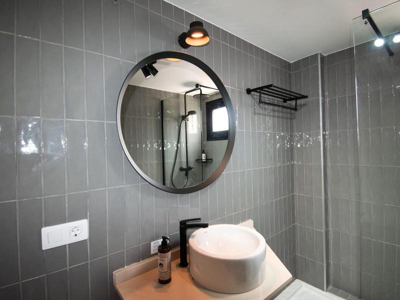 Modernes Badezimmer mit grauen Wandfliesen, rundem Spiegel, Waschbecken und schwarzer Armatur.