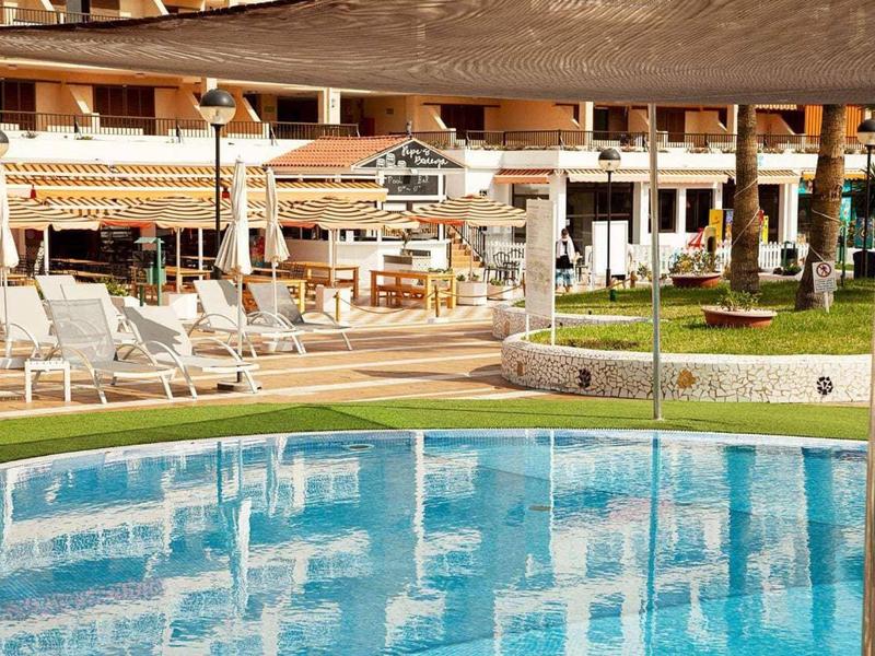 Schwimmbad mit Sonnenschirmen, Liegestühlen und Grasflächen in einem Hotelhof.