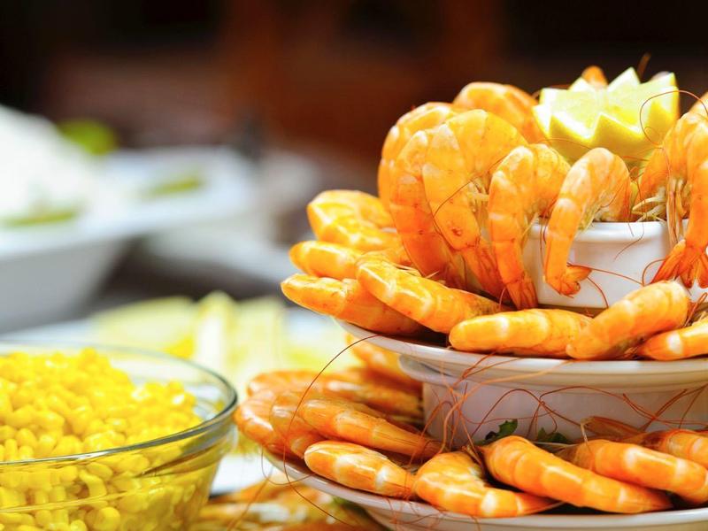 Mehrstöckiger Servierteller mit Garnelen, Zitronen und Sauce, daneben kleine Früchte und eine Schüssel.