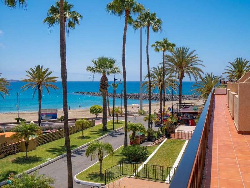 Blick auf eine Promenade mit Palmen, Strand und blauem Meer unter klarem Himmel.