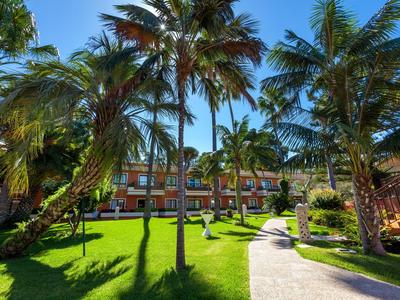 Jardin avec des palmiers et pelouse entretenue devant un bâtiment hôtelier à plusieurs étages par une journée ensoleillée.