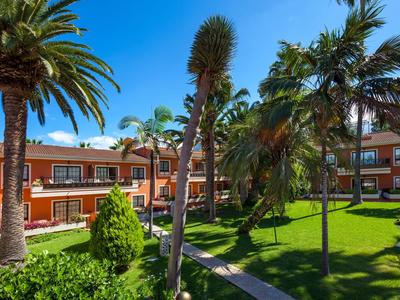 Jardin verdoyant avec palmiers et sentier entre des bâtiments d'hôtel de deux étages sous un ciel clair
