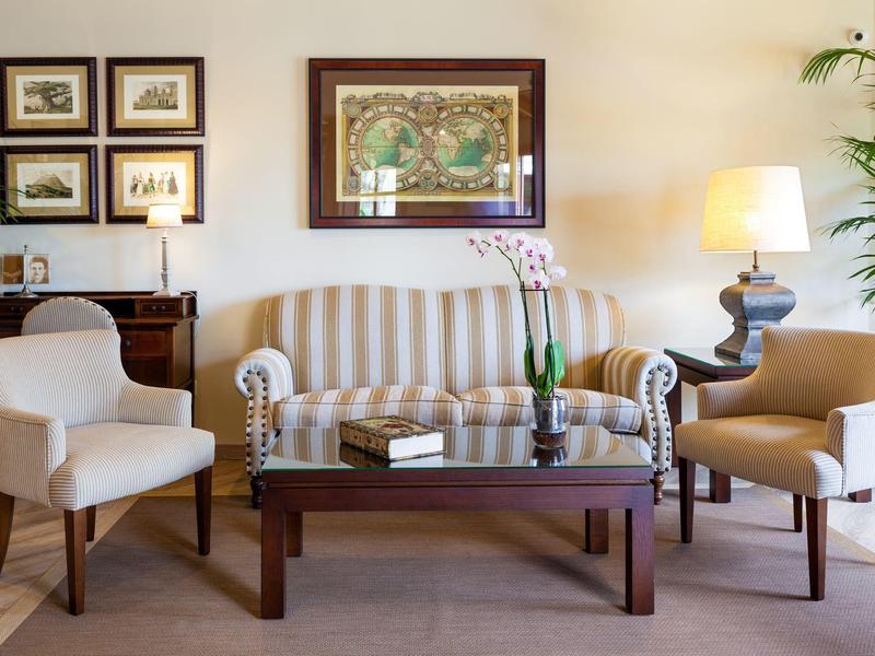 Wohnzimmer mit hellen Möbeln, braunem Holztisch, mehreren Bildern und einer Stehlampe.