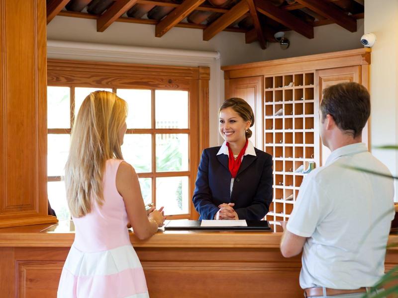 Drei Personen an einer heller Holztresen im Empfangsbereich mit großen Fenstern und sichtbarer Decke.