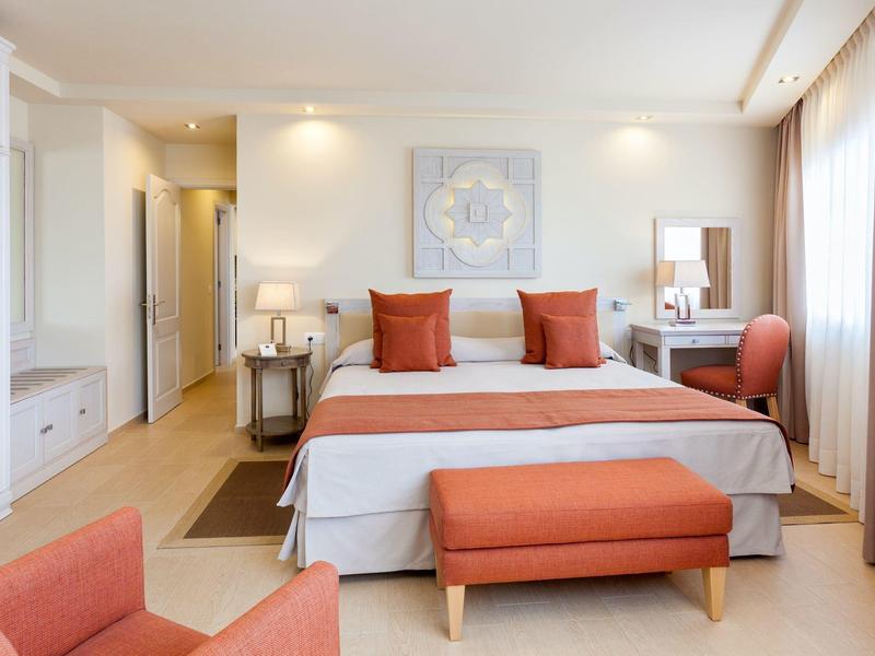 Helles Schlafzimmer mit Doppelbett, orangen Kissen, Sitzbank und einer gemütlichen Ecke.