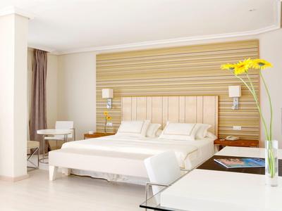 Jasny pokój hotelowy z dużym łóżkiem podwójnym, drewnianą ścianą, biurkiem i żółtym kwiatem.