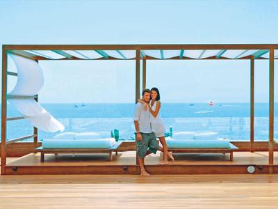 Coppia che si abbraccia su una terrazza in legno con vista sul mare e mobili lounge.