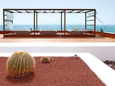 Nowoczesny basen hotelowy z drewnianym tarasem i kaktusami na czerwonym żwirze na pierwszym planie i widokiem na morze.