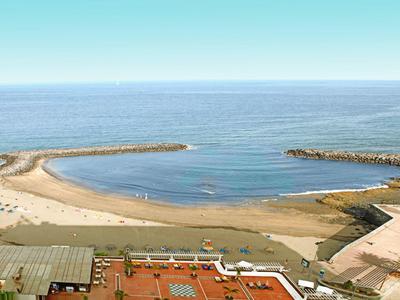 Szeroka piaszczysta plaża otoczona falochronami z pobliskimi budynkami i czystym niebem.