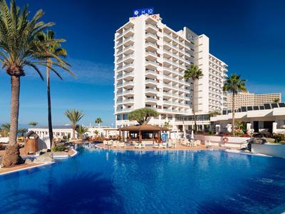 Hotel mit großem Außenpool, Palmen und Sonnenschirmen bei klarem blauem Himmel