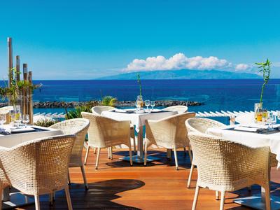 Terrazza con tavoli e sedie con vista sul mare sotto un cielo azzurro con nuvole.