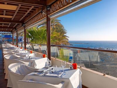 Zadaszony taras z nakrytymi stołami i widokiem na morze w jasną pogodę.