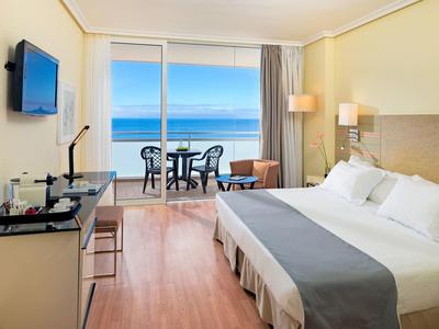 Pokój hotelowy z łóżkiem podwójnym, biurkiem i balkonem z widokiem na morze.