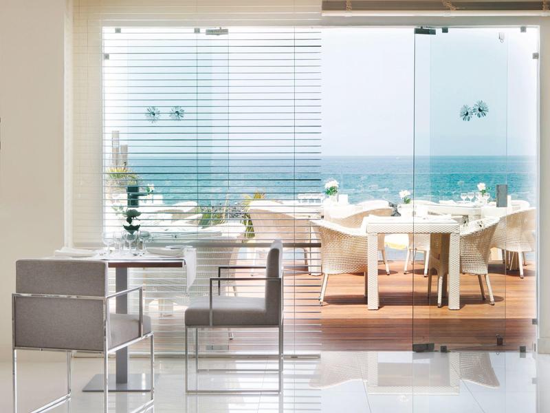 Nowoczesna jadalnia z białymi krzesłami i widokiem na morze przez duże szklane okna.
