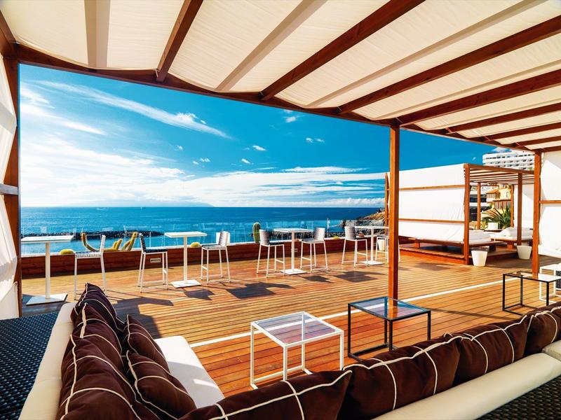 Taras z miejscem do siedzenia i widokiem na morze pod zadaszonym pergolą w słoneczny dzień.