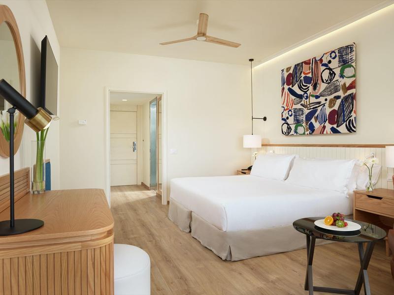 Jasny pokój hotelowy z łóżkiem podwójnym, nowoczesnymi meblami i kolorową dekoracją ściany.