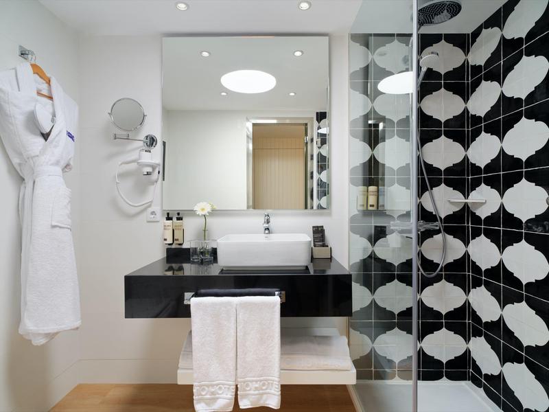 Nowoczesna łazienka hotelowa z umywalką, dużym lustrem i białymi ręcznikami.