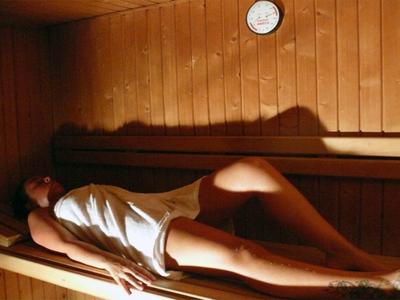 Frau liegt entspannt auf Holzbänken in einer Sauna, mit Handtuch bedeckt, warme Beleuchtung.