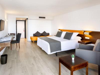 Helles Hotelzimmer mit Doppelbett, grauen Akzenten, Sitzbereich, Schreibtisch und Holzboden.