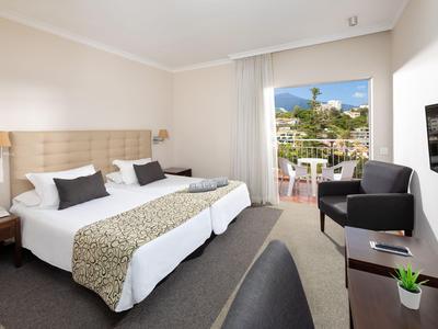 Hell eingerichtetes Hotelzimmer mit zwei Einzelbetten, Sitzbereich und Balkon mit Aussicht.