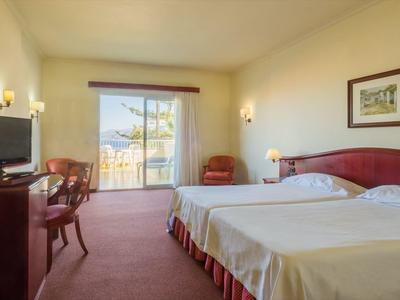 Helles Hotelzimmer mit Doppelbett, Schreibtisch, Fernseher und Balkon mit Bergblick.
