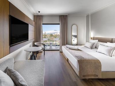 Nowoczesny pokój hotelowy z podwójnym łóżkiem, sofą, telewizorem i balkonem z widokiem na morze.