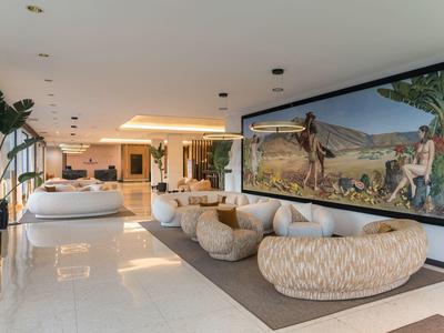Weißer, moderner Hotel-Lobbybereich mit gemütlichen Sofas und großem Wandgemälde.