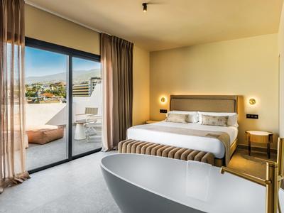Helles Hotelzimmer mit großem Bett, freistehender Badewanne und Zugang zu einer Terrasse mit Aussicht.