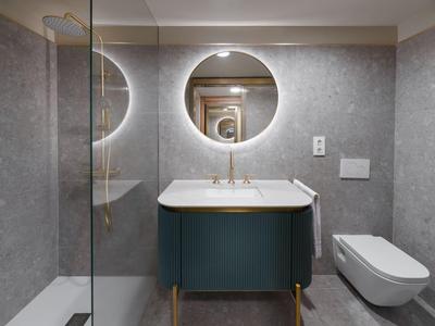Moderner Hotelbadezimmer mit grauen Fliesen, runder Spiegel und blauer Waschtisch.
